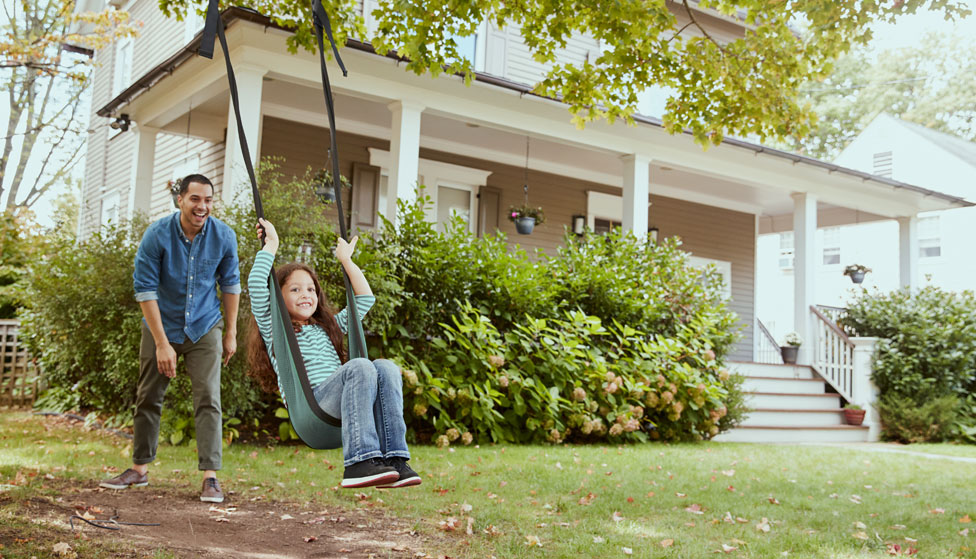 Father pushing daughter on swing in their house front yard Father pushing daughter on swing in their house front yard